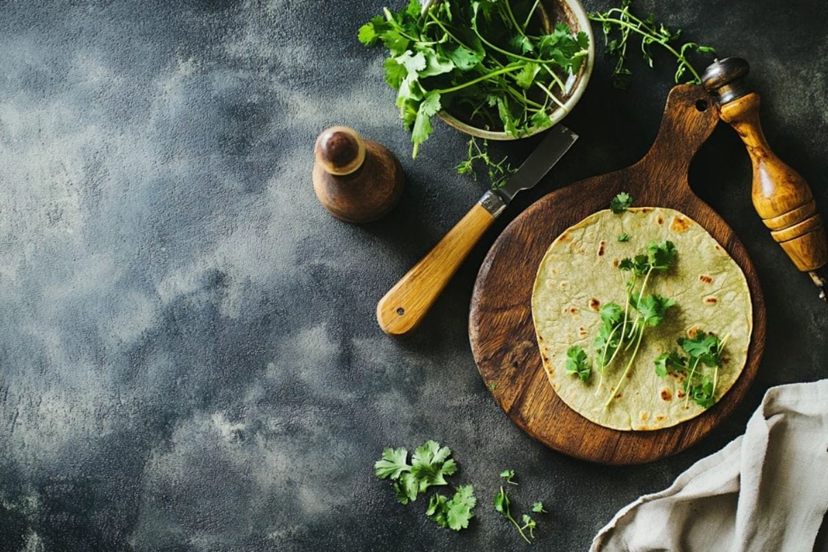 Freshly baked tortillas on a wooden board with a sprinkle of herbs