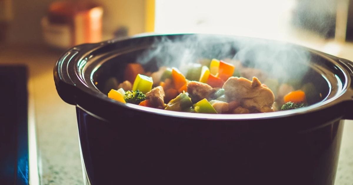 Crockpot cooking a mix of vegetables and meat in a kitchen