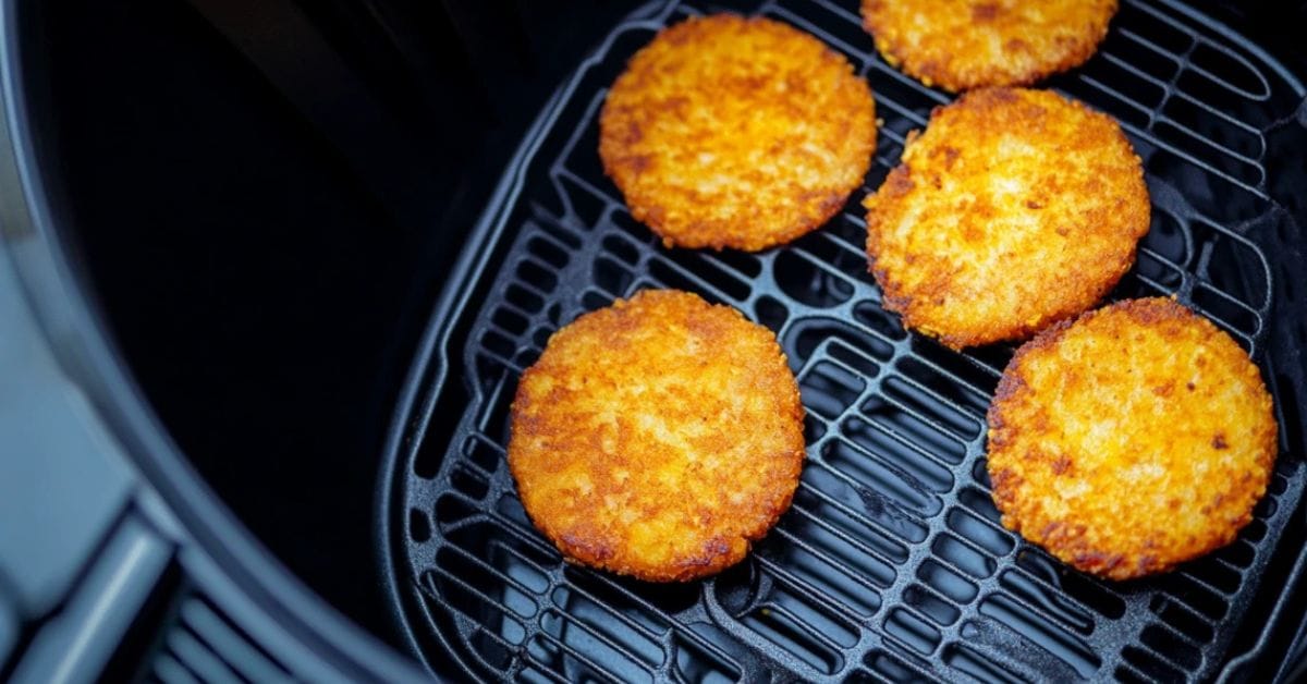 Frozen hash brown patties cooking in an air fryer basket.