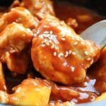 A plate of Sweet Hawaiian Crockpot Chicken served over rice, garnished with sesame seeds and green onions.