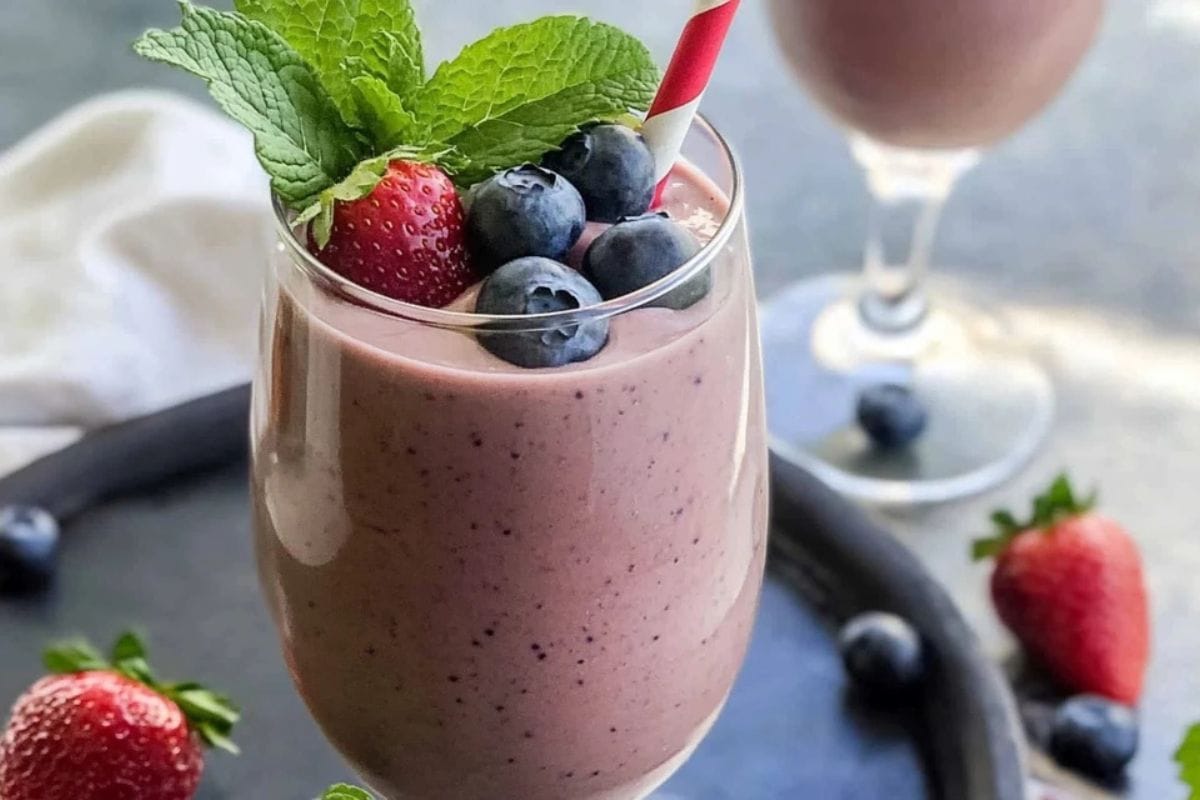 A creamy Greek yogurt smoothie with fresh berries and a mint garnish in a clear glass.